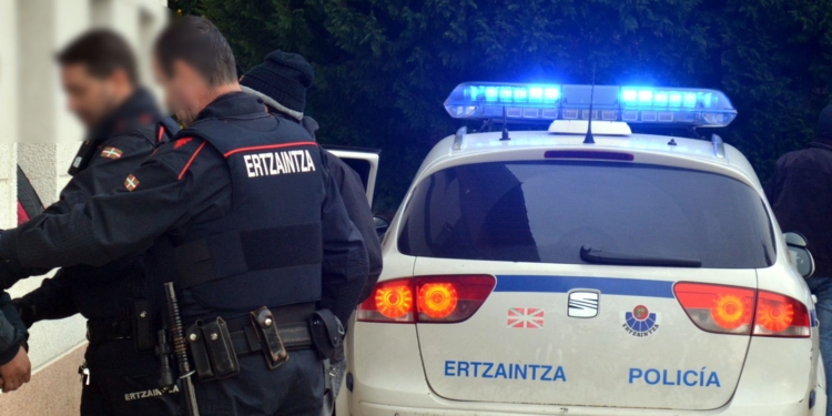 Un senegalés y un latinoamerciano agreden a sus respectivos compañeros de piso. Agentes de la Ertzaintza junto a un vehículo policial con luces azules encendidas.