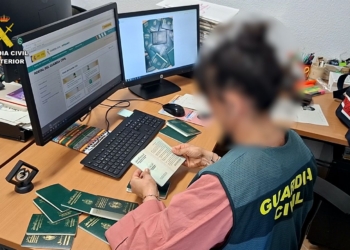 La estafa de la regularización: papeles por dinero. Agente de la Guardia Civil revisa varios pasaportes en una oficina con ordenadores