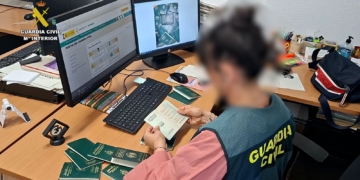 La estafa de la regularización: papeles por dinero. Agente de la Guardia Civil revisa varios pasaportes en una oficina con ordenadores