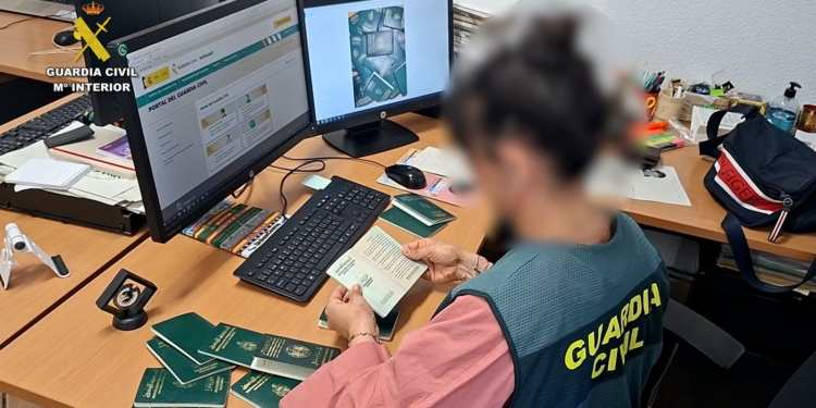 La estafa de la regularización: papeles por dinero. Agente de la Guardia Civil revisa varios pasaportes en una oficina con ordenadores