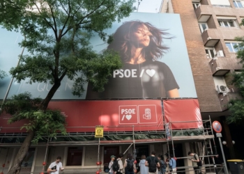 Registro de la UCO en Ferraz: investigan financiación ilegal del PSOE. Fachada de un edificio con una gran lona del PSOE y personas en la acera.
