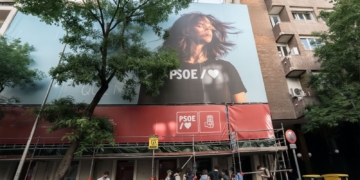 Registro de la UCO en Ferraz: investigan financiación ilegal del PSOE. Fachada de un edificio con una gran lona del PSOE y personas en la acera.