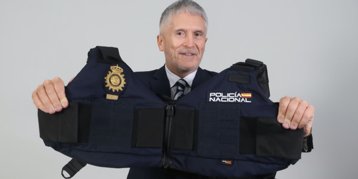 Marlaska expone a 2.600 policías alumnos sin protección en la visita del Papa. Marlaska sostiene un chaleco de la Policía Nacional frente a un fondo neutro.