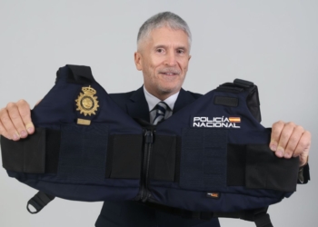 Marlaska expone a 2.600 policías alumnos sin protección en la visita del Papa. Marlaska sostiene un chaleco de la Policía Nacional frente a un fondo neutro.