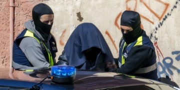 5 ataques yihadistas en pocas horas disparan la alarma en España y Europa. Dos agentes con el rostro cubierto escoltan a una persona tapada con una tela oscura junto a un vehículo policial.