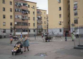 Niña de 10 años herida en tiroteo de clanes en Badalona. Barrio de San Roc Vista de una plaza entre edificios residenciales donde varias personas están reunidas y una mujer empuja un carrito de bebé.