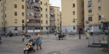 Niña de 10 años herida en tiroteo de clanes en Badalona. Barrio de San Roc Vista de una plaza entre edificios residenciales donde varias personas están reunidas y una mujer empuja un carrito de bebé.