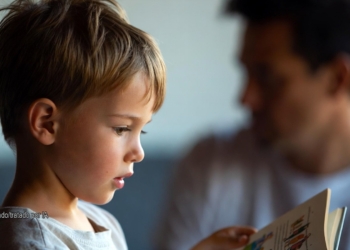 'El semen mola' el libro infantil que indigna a padres en Cataluña. Niño leyendo un libro mientras un adulto aparece desenfocado al fondo