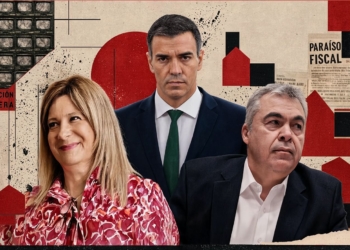 La investigación de la UCO apunta a Pedro Sánchez. Retrato de un hombre con gafas y traje delante de una bandera con franjas rojas y amarillas.