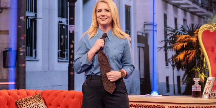 Escándalo en RTVE: desnudo integral de Henar Álvarez en prime time. La presentadora se encuentra de pie en un plató de televisión junto a un sofá rojo y elementos decorativos.