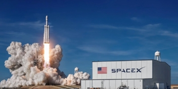 ¿Por qué Elon Musk hace ahora la salida a bolsa de SpaceX?. Lanzamiento de un cohete de SpaceX desde su base, con una gran nube de humo y fuego, junto al edificio principal de la compañía.