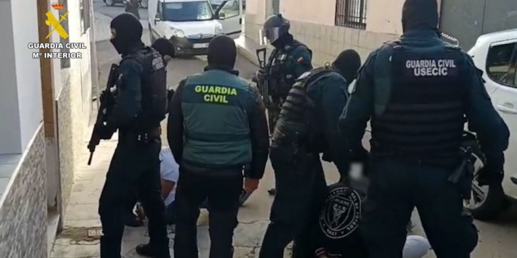 Narcos tirotean a la Guardia Civil en Punta Umbría dejando a los agentes indefensos. Agentes de la Guardia Civil, algunos con pasamontañas y equipamiento táctico, deteniendo a varias personas en el suelo durante una operación policial.