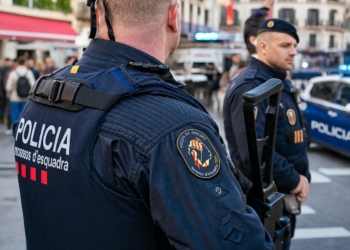 Nueva redada en Barcelona: 13 detenidos, 5 de ellos ilegales por posesión de drogas y tenencia de armas. Agentes de los Mossos d'Esquadra (Policía de Cataluña) en una calle urbana, con un vehículo policial al fondo.