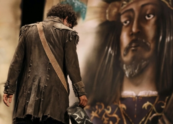 En Cádiz ya se asusta a los niños con "Que viene Juan Carlos". Hombre con traje antiguo y harapiento de espaldas frente a una gran estatua o imagen de un rey coronado.