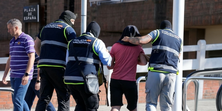 5 nuevos sucesos: la ola de "casos aislados" que sigue azotando España. Agentes de la Policía Nacional escoltando a una persona con la cabeza cubierta en la Plaza de España.